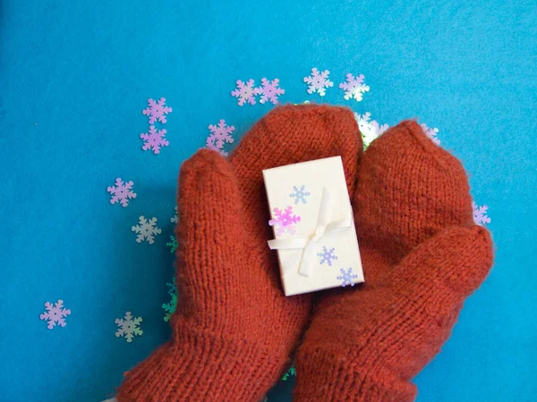 Eldivenli eller, Noel hediyeli eldivenler, mavi arka planda beyaz bir hediye kutusu. Yeni yıl, kış doğum günü. Noel kavramı. Üst görünümü metin için alan.