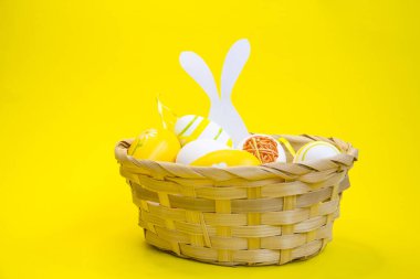 Hasır sepette renkli Paskalya yumurtaları ve sarı, yeşil arka planda ahşap bir kutu. Metin için boşluk