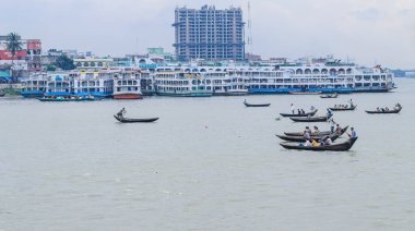 Dhaka 'daki Buriganga nehri üzerindeki Sadarghat nehir limanının güzel manzarası. Nehirde bulutlu bir arka planı olan feribotlar..