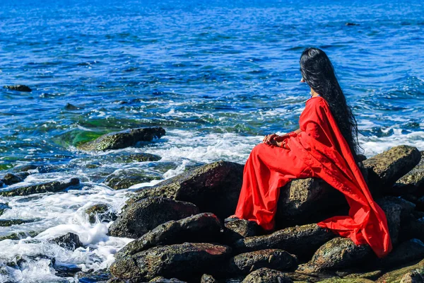 Young women wearing a red saree on the beach. Girl in traditional Indian sari among the rocks and enjoying the freedom and the sunset or sunrise. Beautiful Indian woman on the beach wearing a sari.