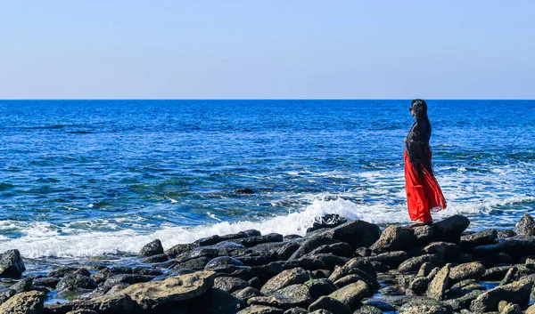 Young women wearing a red saree on the beach. Girl in traditional Indian sari among the rocks and enjoying the freedom and the sunset or sunrise. Beautiful Indian woman on the beach wearing a sari.