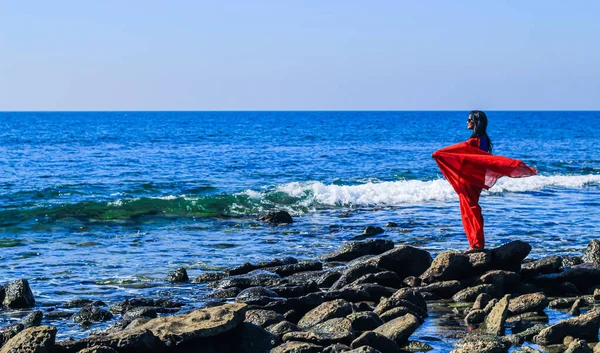 Young women wearing a red saree on the beach. Girl in traditional Indian sari among the rocks and enjoying the freedom and the sunset or sunrise. Beautiful Indian woman on the beach wearing a sari.