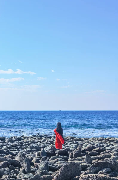 Young women wearing a red saree on the beach. Girl in traditional Indian sari among the rocks and enjoying the freedom and the sunset or sunrise. Beautiful Indian woman on the beach wearing a sari.