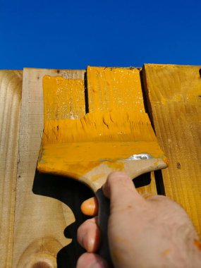 Baharın başında tahta bir çite boya fırçasıyla turuncu bacaklar uygulanacak. temizleme süreci.