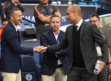 MANCHESTER, ENGLAND - 24 AUGSTOS 2016: Şehir yöneticisi Josep Guardiola (R), Etihad Stadyumu 'nda oynanan 2016 / 17 UEFA Şampiyonlar Ligi ikinci ayağı öncesinde FCSB yetkilisi Mihai Stoica' yı (L) karşıladı. Polis.