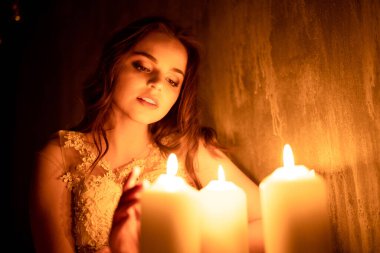 Bir kadın mum ışığında bir odada oturuyor. Genç bir kız yanan mumlara bakar ve nişanlısına şaşar.