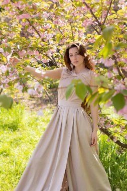 Çiçekli bir sakura bahçesinde poz veren güzel genç bir kadın.