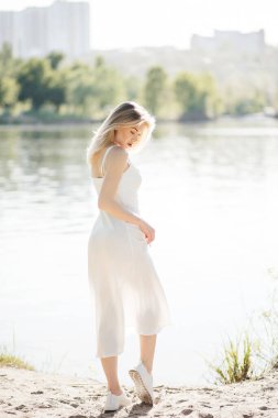 Genç bir kadın nehrin yanında duruyor. Beyaz kanat çırpan elbise içinde güzel bir manken.