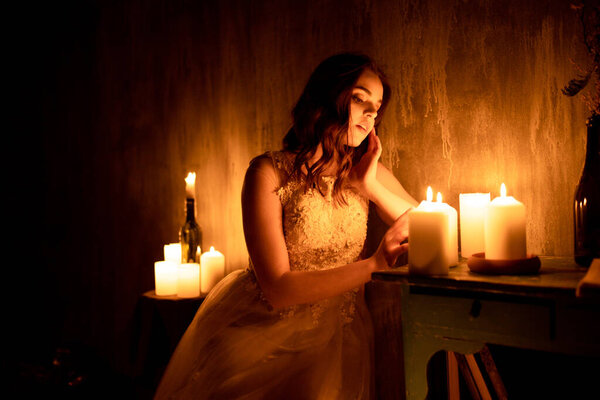 A woman is sitting in a room by candlelight. A young girl looks at burning candles and wonders at her betrothed