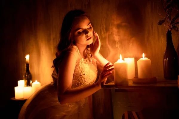 女性がろうそくの明かりで部屋に座っている 若い女の子は燃えるろうそくと不思議を見ます彼女のBetroed ストック画像