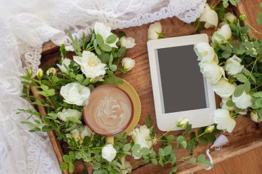 Morning cup of coffee, e-book and beautiful white roses on wooden tray, top view. Cozy breakfast. Flat style.