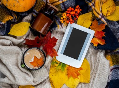 Autumn home cozy composition with checkered plaid, warm sweater, cup of coffee, fall leaves and e-book with copy space. Fall season template for feminine blog social media.