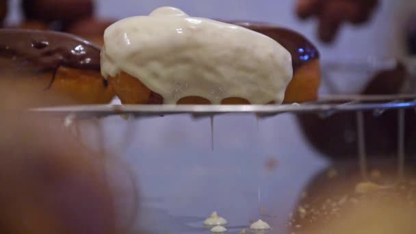 Donut aromatisé à la vanille goutte l'excès de glaçure blanche sur le support de refroidissement. gros plan — Video