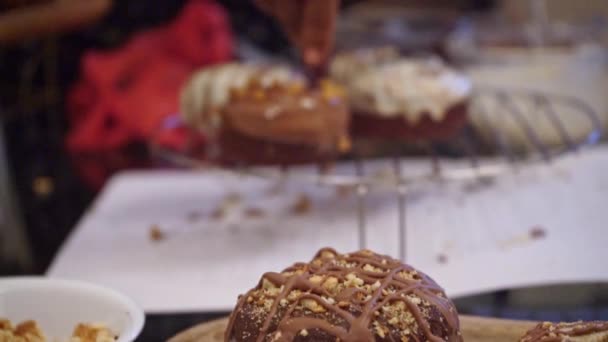 Piekarz posypuje oszklone pączki orzechami na stojaku chłodzącym. średni strzał — Wideo stockowe