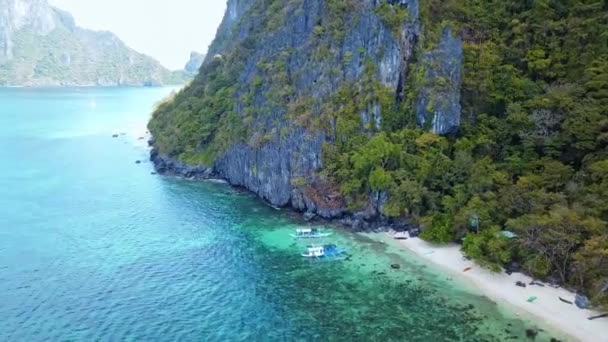 Barcos tradicionales flotando en agua azul turquesa a lo largo de la playa de arena en Moalboal, Filipinas. - antena — Vídeos de Stock