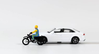 Minyatür bir sürücü beyaz bir minyatür arabanın yanında kask takıyor ve motosiklet sürüyor. Minyatür insanlar ve minyatür arabalar..