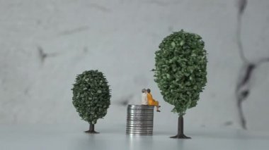 Minyatür ağaçlar arasında madeni paraların üzerinde yaşlanmış minyatür insanlar. Yaşlanan toplum kavramı ve yükselen sosyal maliyetler.