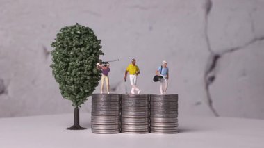 Bozuk para ve minyatür bir ağacın üzerinde duran minyatür golfçüler. Ticari kavramları olan minyatürler ve madeni para yığınları. 