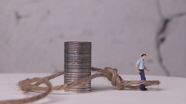 コインとロープの山で織られたミニチュアの男 経済的困難の概念 — ストック動画