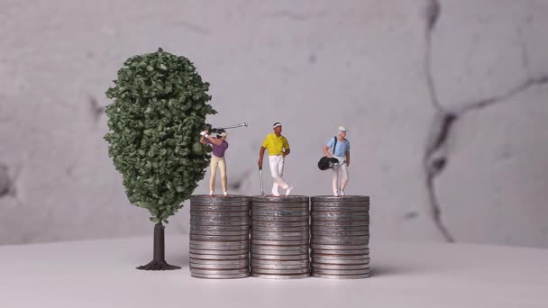 ミニチュアゴルファーはコインとミニチュアツリーの山の上に立っている 事業の概念を有する硬貨のミニチュア及び山 — ストック動画