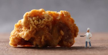 Bir parça kızarmış tavuk ve minyatür bir şef. İş konsepti olan tavuk yemekleri ve minyatür insanlar..