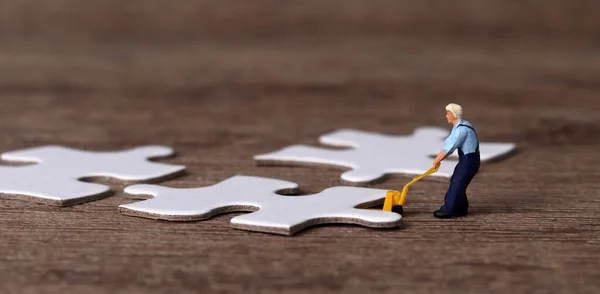 White puzzle pieces and miniature people with business concept. A miniature man carrying a puzzle.