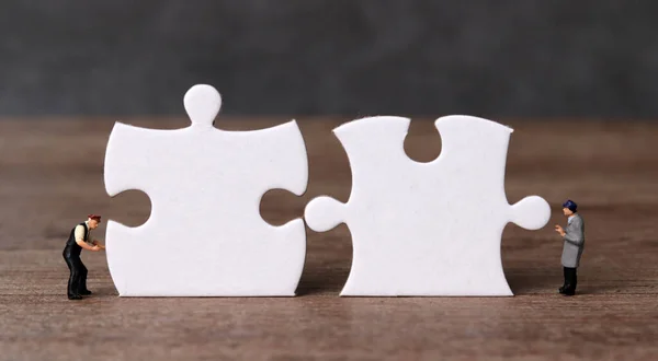 White puzzle pieces and miniature people with business concept. Miniature people working on two pieces of the puzzle.