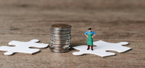 White puzzle pieces and miniature people with business concept. Pile of coins and a miniature man standing on a puzzle.