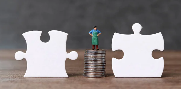 White puzzle pieces and miniature people with business concept. Two pieces of puzzle and a miniature man standing on a pile of coins.