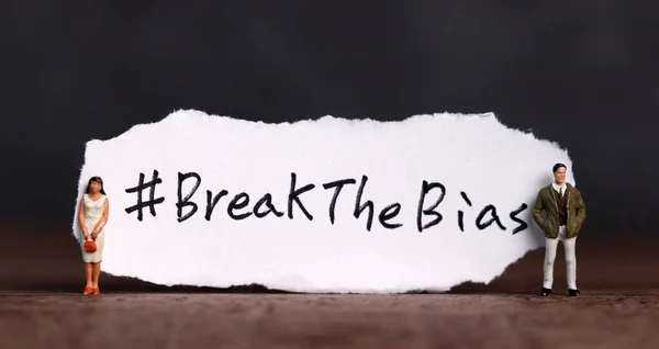 Torn paper with the word \'#BreakTheBias\' written on it. Break the bias campaign with miniature people.