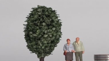 Miniature people and the concept of an aging society. A miniature old couple standing next to a pile of step coins.