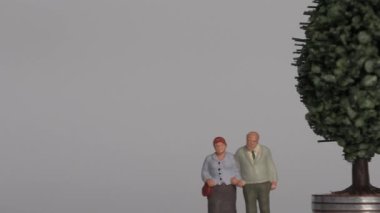 Miniature people and the concept of an aging society. A miniature old couple standing next to a pile of step coins.
