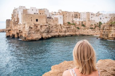 Karabasan Polignano. Kayalıklardaki kasaba, Puglia bölgesi, İtalya, Avrupa. Eski geleneksel evleri, dramatik gökyüzünü, Akdeniz 'i ve sarışın turist kızı içeren seyahat konsepti.