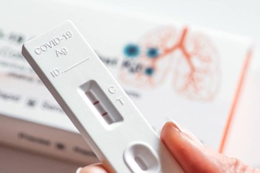 Pozitif Covid-19 antijen test kiti, bir basamak koronavirüs antijen hızlı testi, tükürük çubuğu, akciğer ve sonuçları kontrol eden bir kızın parmaklarının olduğu bir test kutusu. 