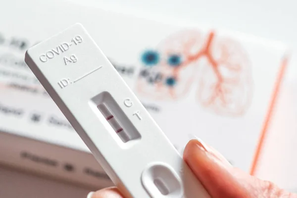 Pozitif Covid-19 antijen test kiti, bir basamak koronavirüs antijen hızlı testi, tükürük çubuğu, akciğer ve sonuçları kontrol eden bir kızın parmaklarının olduğu bir test kutusu. 