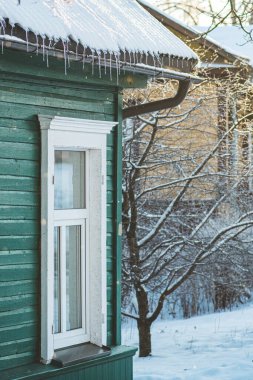 Kış sarkıtları, Trakai, Vilnius, Litvanya 'da dikey beyaz pencereli eski ahşap bir evin karıyla kaplı bir çatıdan sarkıyor.