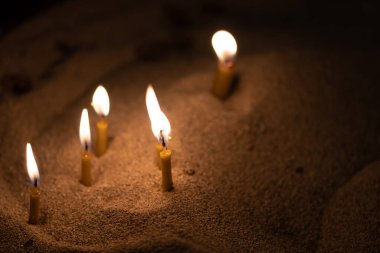 Dağılmış mumlar kumda altın sarısı bir ışıkla parlıyor, boşluğu kopyala