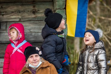 Vilnius, Litvanya - 2 Mart 2022: Rusya 'nın işgali sırasında Ukrayna bayrağı taşıyan ahşap bir evin yanında büyükannesi olan güzel Ukraynalı çocuklar ve çocuklar, savaş mültecileri