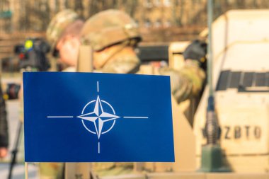 Vilnius, Litvanya - 29 Mart 2022: NATO bayrağı ve sembolü, odak dışı askerleri ve zırhlı araçları olan zorla entegrasyon birimi