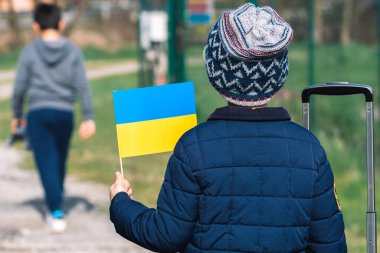 Ukrayna 'daki savaş sırasında Putin ve Rusya' nın, mültecilerin, mültecilerin kampının neden olduğu kışlık giysileri, şapkası ve Ukrayna bayrağı taşıyan çocuklar veya çocuklar.