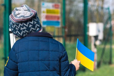 Ukrayna 'daki savaş sırasında Putin ve Rusya' nın, mültecilerin, mültecilerin kampının neden olduğu kışlık kıyafetleri, şapkası ve Ukrayna bayrağı taşıyan çocuk ya da çocuk.