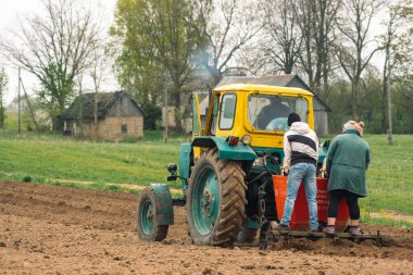 Preili, Letonya - 14 Mayıs 2022: Eski geleneksel ahşap evlerle birlikte baharda eski bir tarım tarlası Belarus ile toprağı sürme ve ekme