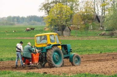 Preili, Letonya - 14 Mayıs 2022: Eski geleneksel ahşap evlerle birlikte baharda eski bir tarım tarlası Belarus ile toprağı sürme ve ekme