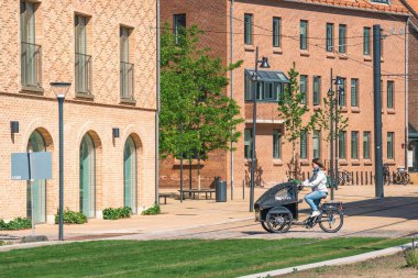 Odense, Danimarka - 23 Mayıs 2022: Odense, Danimarka 'da bahar veya yaz aylarında modern binalar arasında yeni bir bisiklet yolu veya yol üzerinde kargo motosikletli kız veya kadın