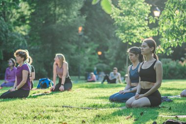 Vilnius, Litvanya - 22 Haziran 2022: Güzel kızlar yaz aylarında halka açık bir parkta çimlerin üzerinde yoga ya da spor yapıyorlar