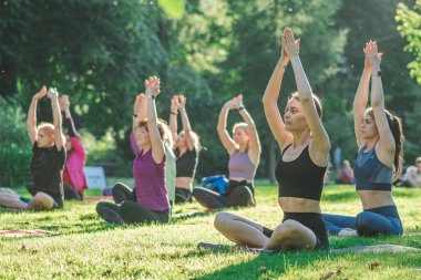Vilnius, Litvanya - 22 Haziran 2022: Güzel kızlar yaz aylarında halka açık bir parkta çimlerin üzerinde yoga ya da spor yapıyorlar
