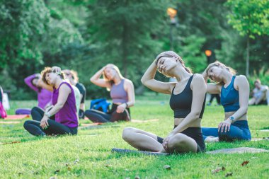 Vilnius, Litvanya - 22 Haziran 2022: Güzel kızlar yaz aylarında halka açık bir parkta çimlerin üzerinde yoga ya da spor yapıyorlar