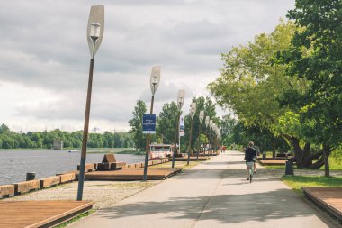 Parnu, Estonya, Avrupa - 19 Haziran 2022: Parnu nehri boyunca bisiklet süren ve arka planda bulutlu gökyüzü olan kız