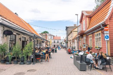 Parnu, Estonya, Avrupa - 19 Haziran 2022: Geleneksel evleri ve restoranların masalarında oturan insanlar ile Parnu eski kasaba caddesi