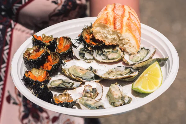 Tourist showing a plate with raw sea urchins and oysters ready to eat with bread and lemon in Bari, Puglia, Italy